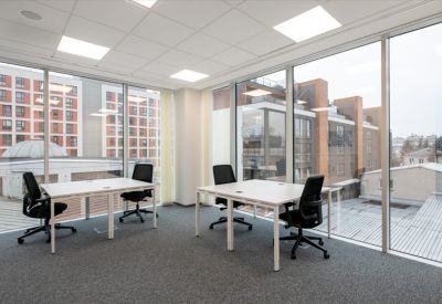 Bright corner office suite with white desks and floor-to-ceiling windows showing city architecture.