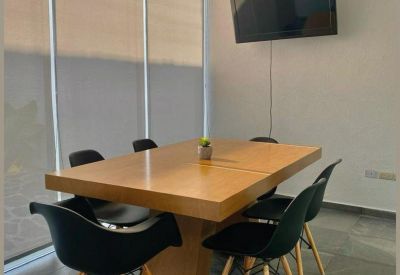 Bright meeting room with a large wooden table, black chairs, and a wall-mounted television.