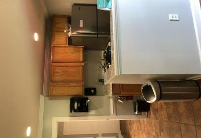 Communal kitchen area with wooden cabinetry and stainless steel refrigerator.