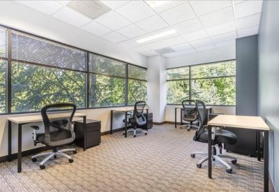 Open-plan office with several desks and large windows.