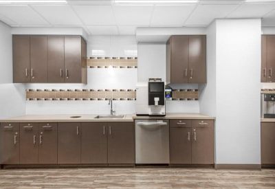 Modern office kitchen with brown cabinetry and integrated coffee machine.