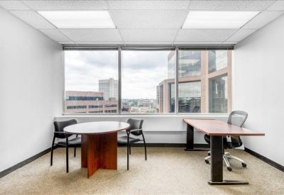 Bright corner office with a round wood meeting table and window views.