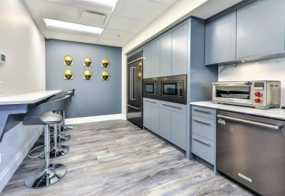 Modern office kitchen with blue cabinetry, stainless steel appliances, and breakfast bar seating.