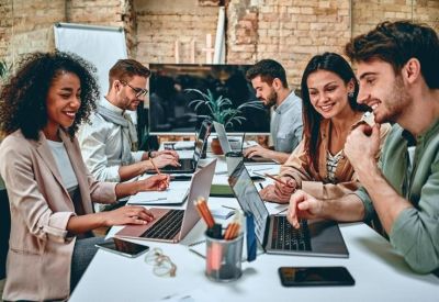 Modern open-plan office featuring several rows of white desks with multiple computer monitors.