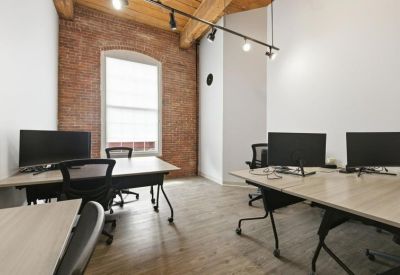 Bright corner office with exposed brick walls, timber ceilings, and multiple workstations.