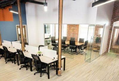 Open-plan office with white desks, ergonomic chairs, and industrial wooden pillars.