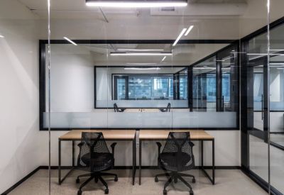 Private glass-walled office suite with two minimal wood desks and ergonomic chairs.