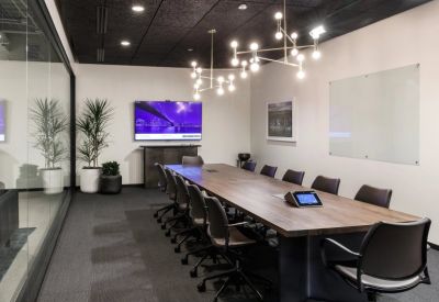 Modern conference room with a long wood table, designer light fixture, and large wall monitor.