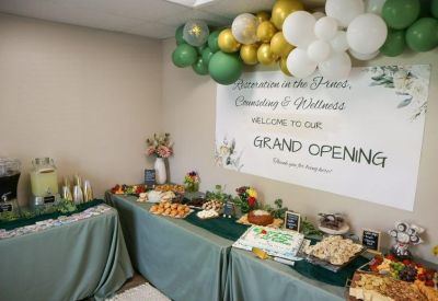 Communal break area with a grand opening banner, green and gold balloons, and a buffet of snacks.