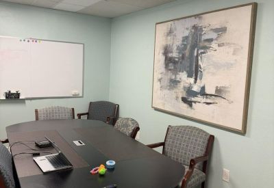 Professional meeting room with a long dark wood table, gray patterned chairs, and a whiteboard.