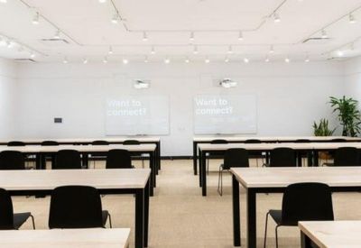 Bright classroom-style meeting room with rows of white desks and black chairs.