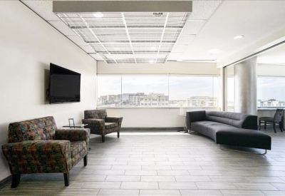 Sunlit lounge area with comfortable armchairs, a sofa, and large windows.