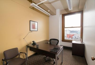 Private office suite with a wood desk, ergonomic chair, and city views through a large window.