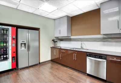 Modern office kitchen with wood-tone cabinetry and a full-size refrigerator.