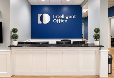 Branded reception area with a white paneled desk, blue feature wall, and manicured topiaries.