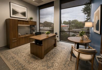 Spacious private office featuring a large wooden desk, patterned rug, and floor-to-ceiling windows.