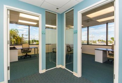 Bright glass-walled private offices with teal carpets and views of the surrounding city.