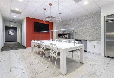 Sleek communal kitchen and breakout area with a long white dining table and red accent wall.