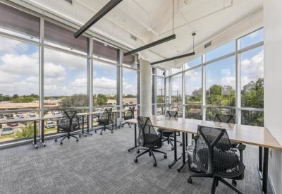 Modern office space with multiple desks and ergonomic chairs facing floor-to-ceiling windows.