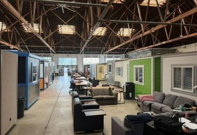 Communal lounge area with a grey sectional sofa and rows of micro-offices.