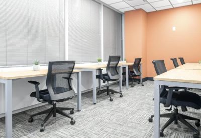 Open-plan coworking area with rows of wooden desks and black mesh chairs against an orange accent wall.