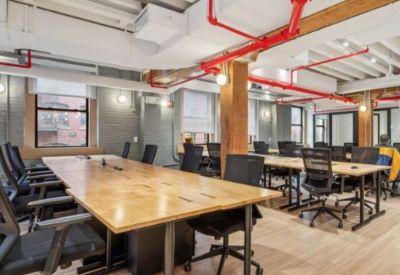 Modern open-plan office space with light wood desks and black ergonomic chairs.