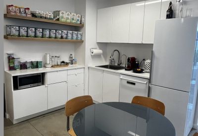 Communal kitchen area with white cabinetry, wooden shelving, and a small dining table.