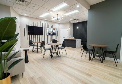 Open coworking space with several round tables, black chairs, and a kitchen area.