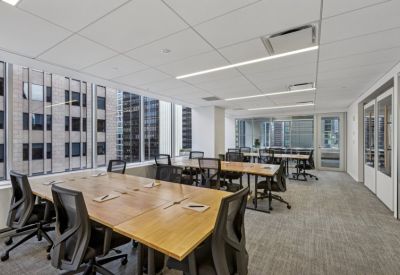 Sunlit open-plan workspace with long wooden tables and views of surrounding Manhattan architecture.