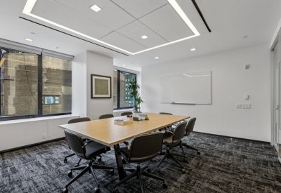 Minimalist conference room with a light wood table, black ergonomic chairs, and a whiteboard.