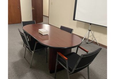 Professional meeting room with an oval mahogany table, chairs, and a projection screen.