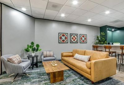 Modern lounge area with a tan leather sofa, grey armchairs, and colorful wall art.