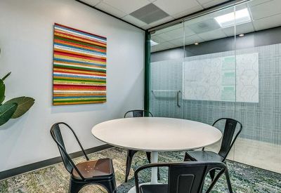 Small meeting room with a round white table, black chairs, and vibrant striped wall art.
