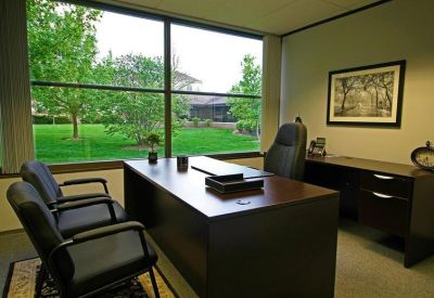 Private office with a dark wood desk and large window overlooking greenery.