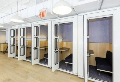 Row of private, soundproof white phone booths with glass doors and wood interior accents.