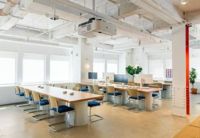 Large meeting area with long wooden tables, blue chairs, and a ceiling-mounted projector.