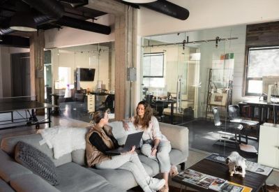 Lounge area featuring two people on a gray sofa using a laptop in an industrial-style office.
