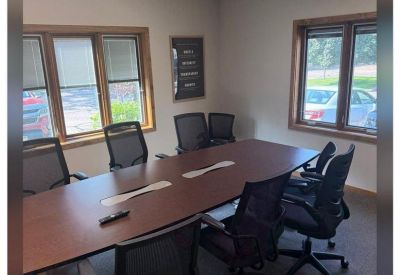 A professional conference room with a long wood table, black mesh chairs, and large windows.