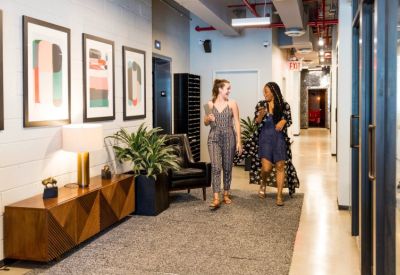 Bright office hallway with framed abstract art, a leather armchair, and a decorative wooden sideboard.