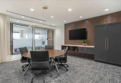 Modern meeting room with a round wooden table and wall-mounted screen.
