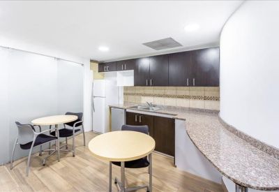 Communal kitchen and dining area with dark cabinetry, granite counters, and small tables.