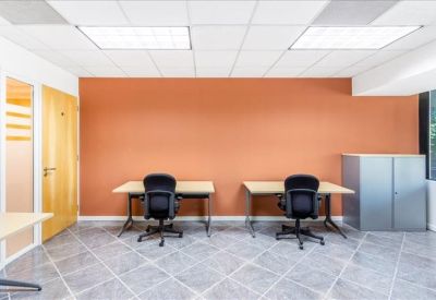 Two-person workspace with desks and black office chairs against a terracotta feature wall.