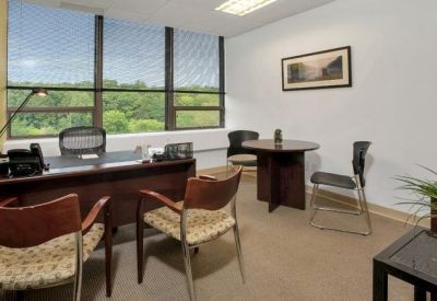 Private windowed office with a dark wood desk and grey guest chairs.