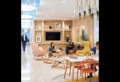 Brightly lit modern coworking space with diverse seating and a large digital screen.