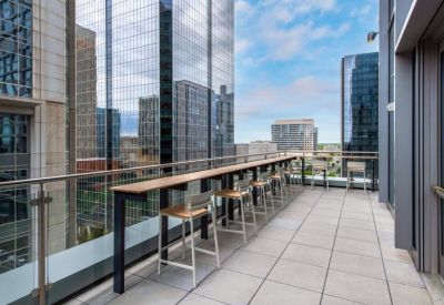 High-rise rooftop balcony with a long wooden bar table and views of city skyscrapers.