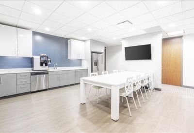 Modern breakroom kitchen with grey cabinetry, stainless steel appliances, and a long white dining table.