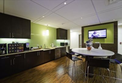 Modern breakroom kitchen with dark cabinetry, green accent walls, and a white cafe table.