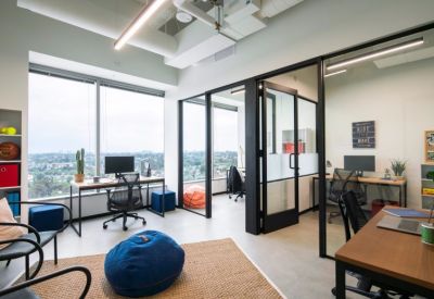Bright office with individual desks, ergonomic chairs, and glass-walled private suites.