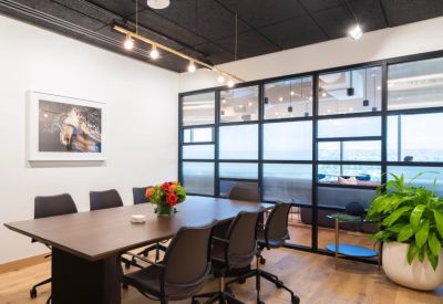 Modern meeting room with a dark wood table, black leather chairs, and frosted glass partitions.