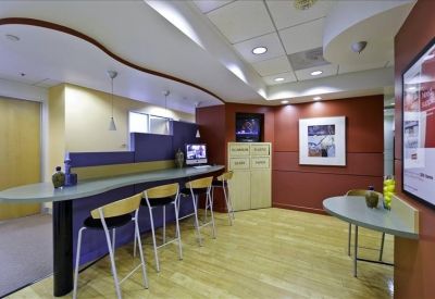 Modern breakroom area with a curved breakfast bar, barstools, and wood-style flooring.